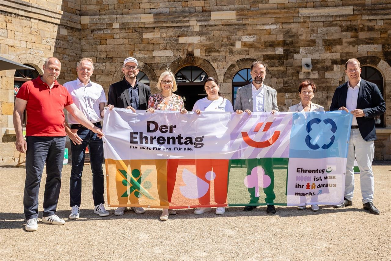 Auf dem Bild sind acht Personen zu sehen, die Einen Banner vor sich halten, welcher auf das Event hinweist.